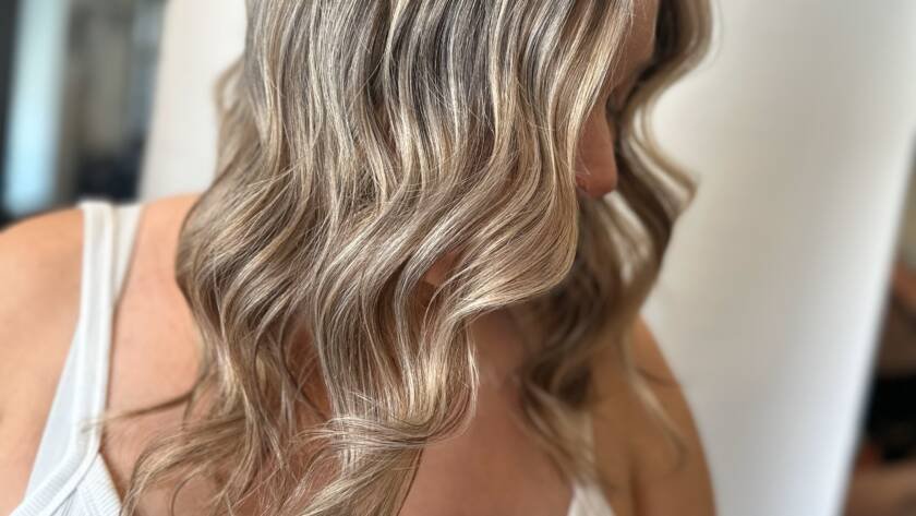 A woman with sun-kissed wavy hair showcasing Redken Shades EQ highlights and balayage.